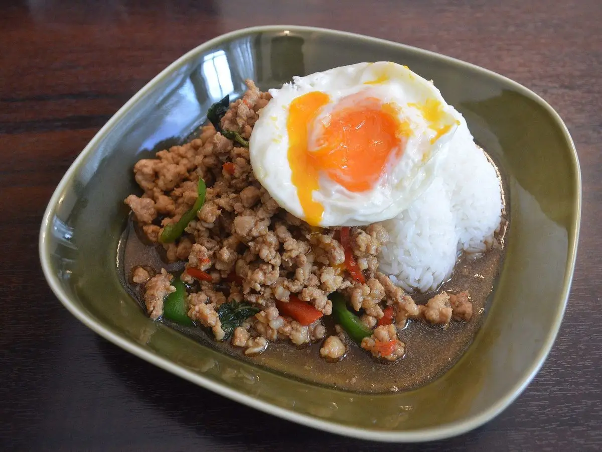 Carne picada salteada con albahaca sobre arroz con un huevo frito, servido en un plato hondo