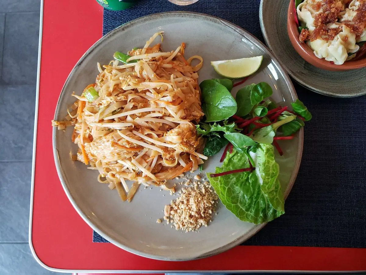 Pad thai con brotes de soja, lima, hojas verdes y cacahuetes triturados en un plato gris