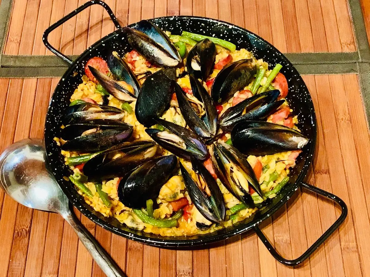 Paella con mejillones y arroz amarillo en una paellera negra sobre una mesa de madera