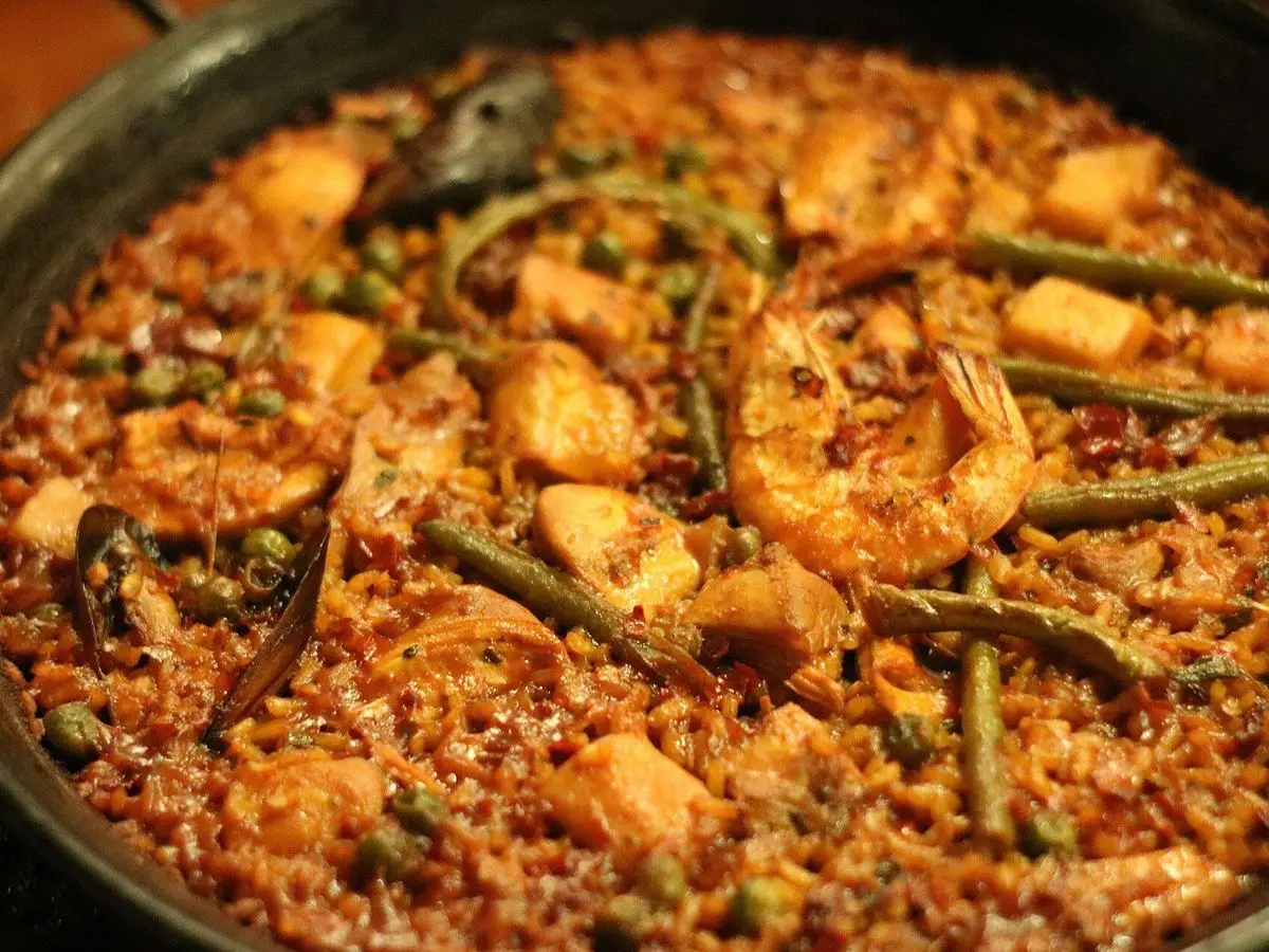 Paella mixta en sartén con arroz dorado, trozos de pollo, gamba y judías verdes