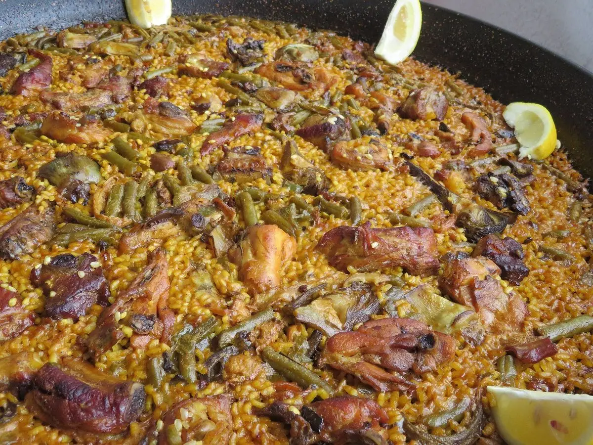 Paella grande con arroz, trozos de pollo y conejo, judías verdes y rodajas de limón
