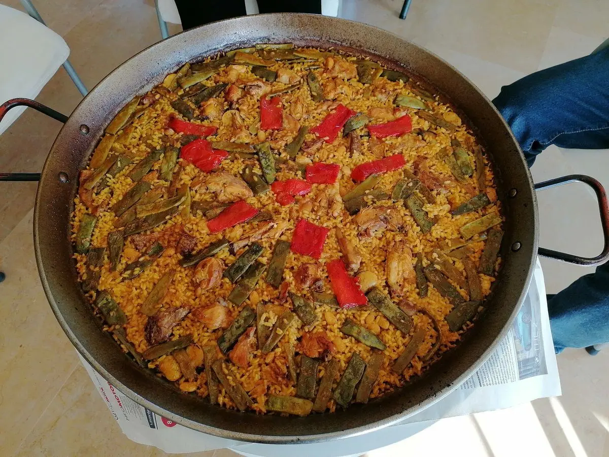 Paella grande en su paellera con arroz, pimiento rojo y verduras