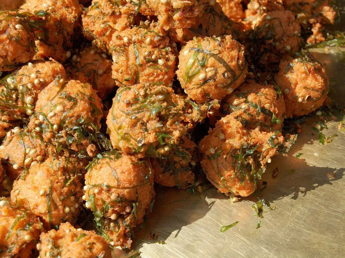 Pakoras redondos y dorados fritos con hierbas amontonados sobre una superficie de madera