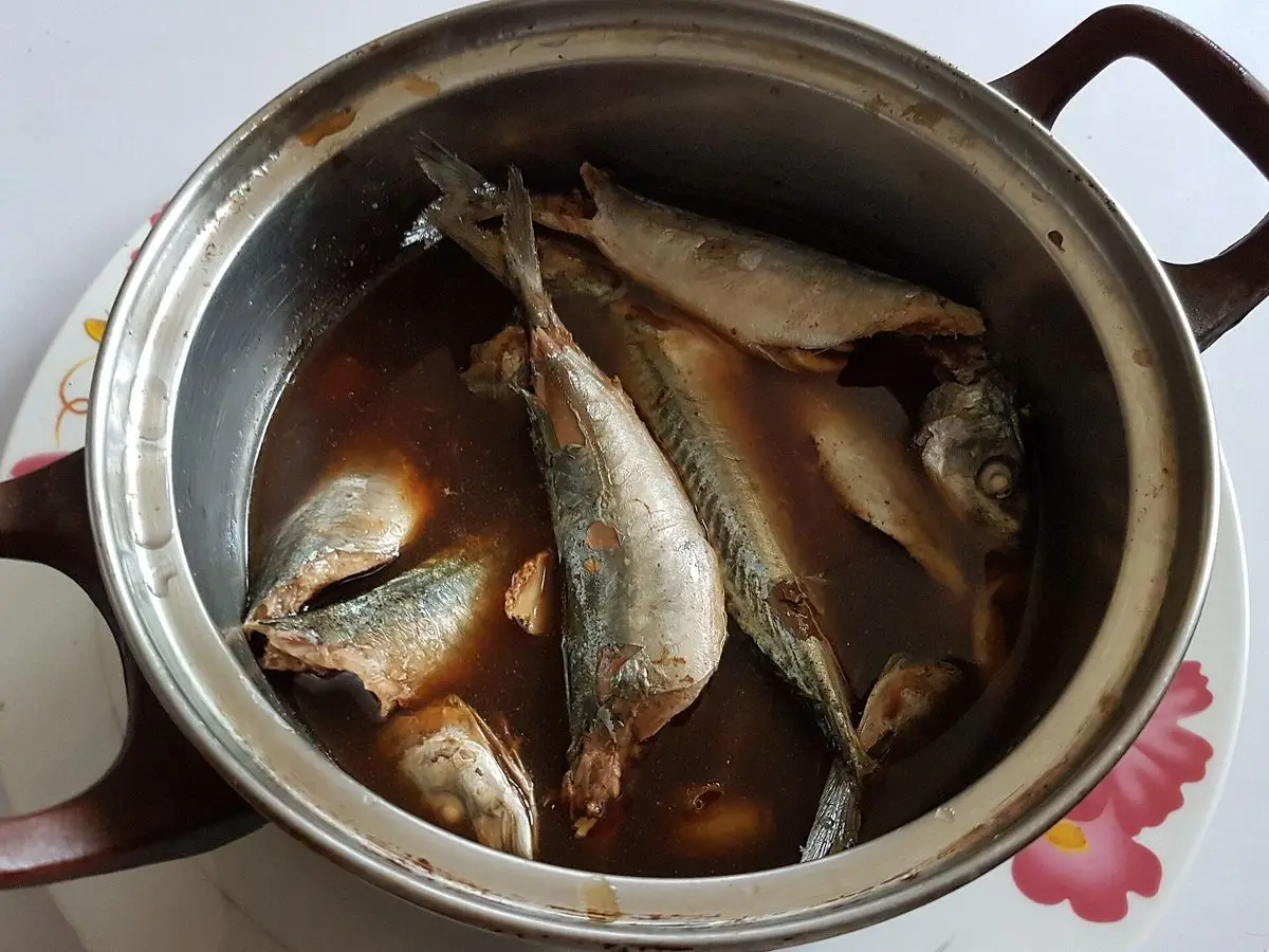 Olla metálica con pescados enteros guisados en salsa oscura de vinagre