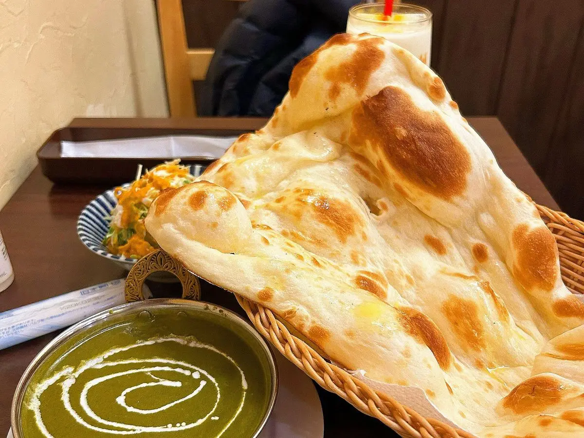 Cuenco de curry cremoso de espinacas con nata junto a un pan naan en una cesta