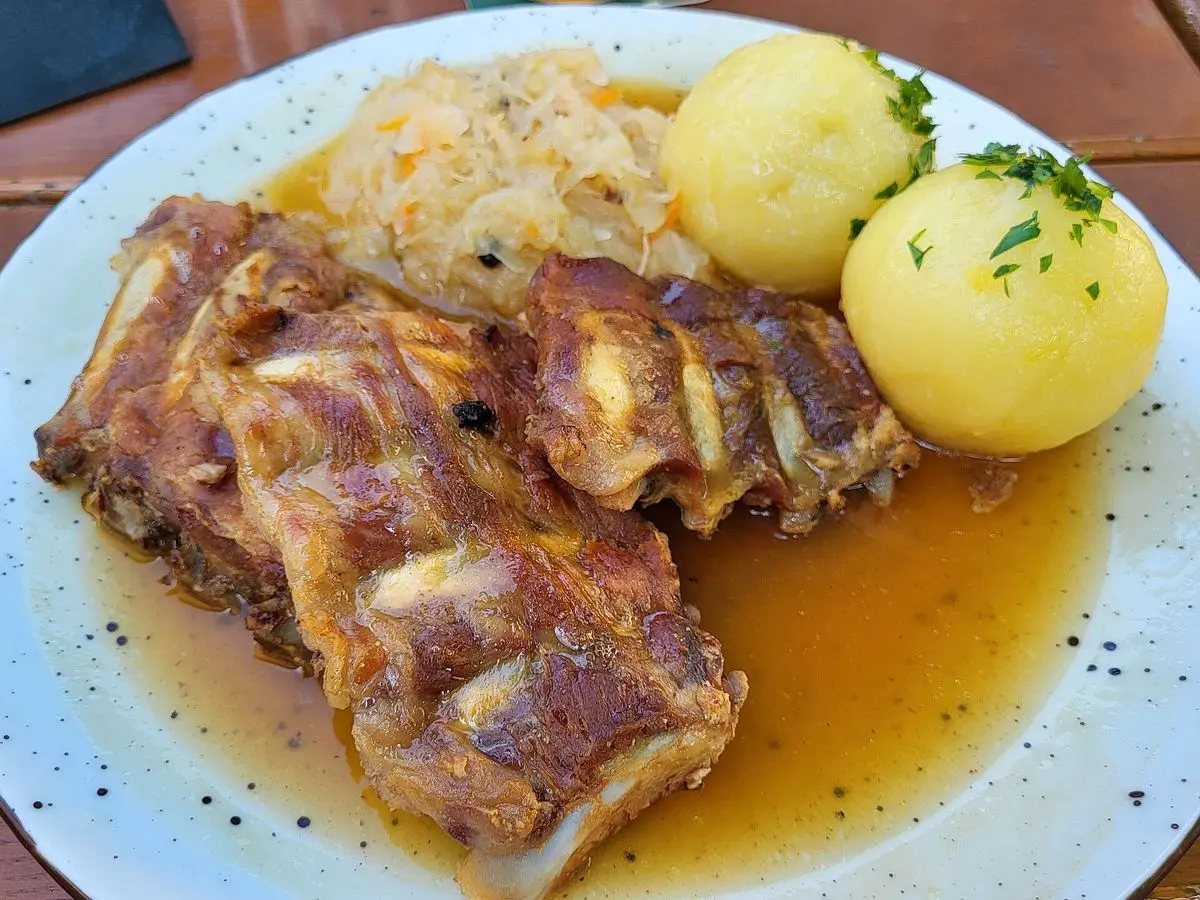 Carne de cerdo asada con chucrut, patatas con perejil y salsa en un plato blanco
