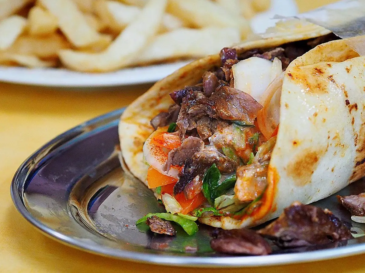 Pan de pita relleno de carne de cordero desmenuzada con tomate, cebolla y salsa, con patatas fritas