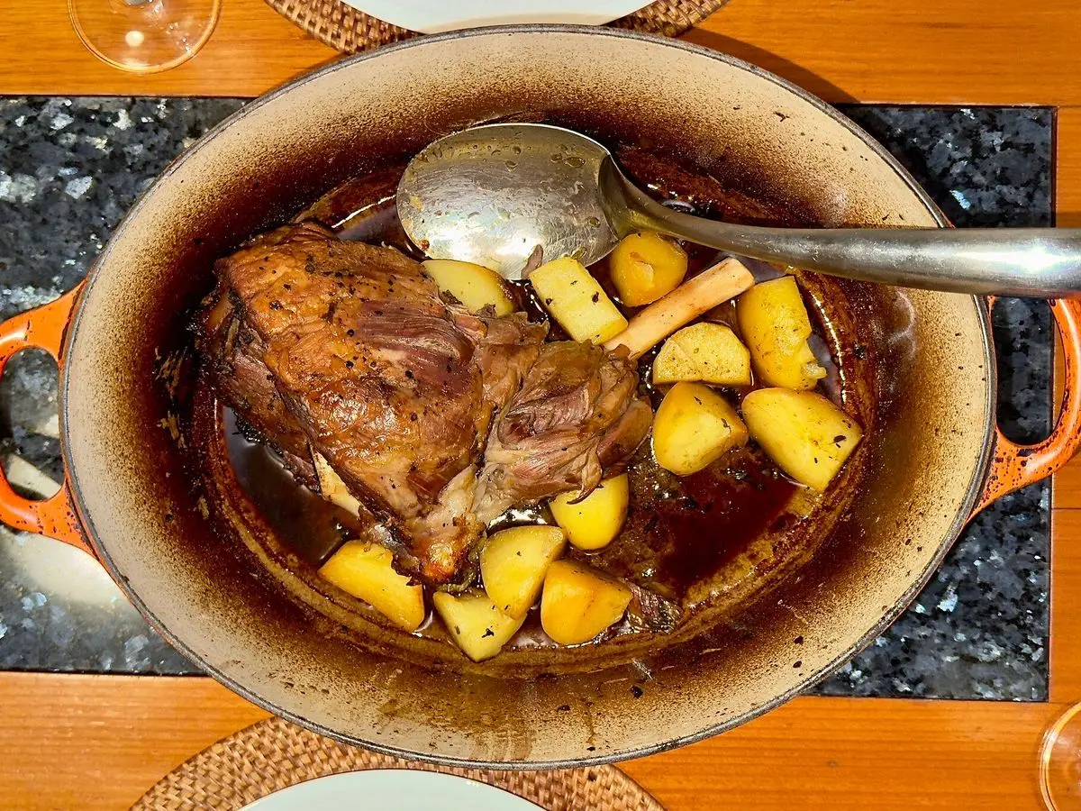 Cazuela roja con paletilla de cordero asada y patatas doradas con una cuchara
