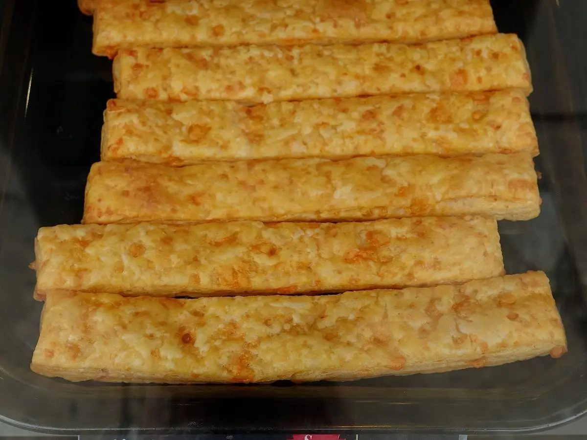 Palitos de hojaldre con queso dorados y alargados, apilados en hileras
