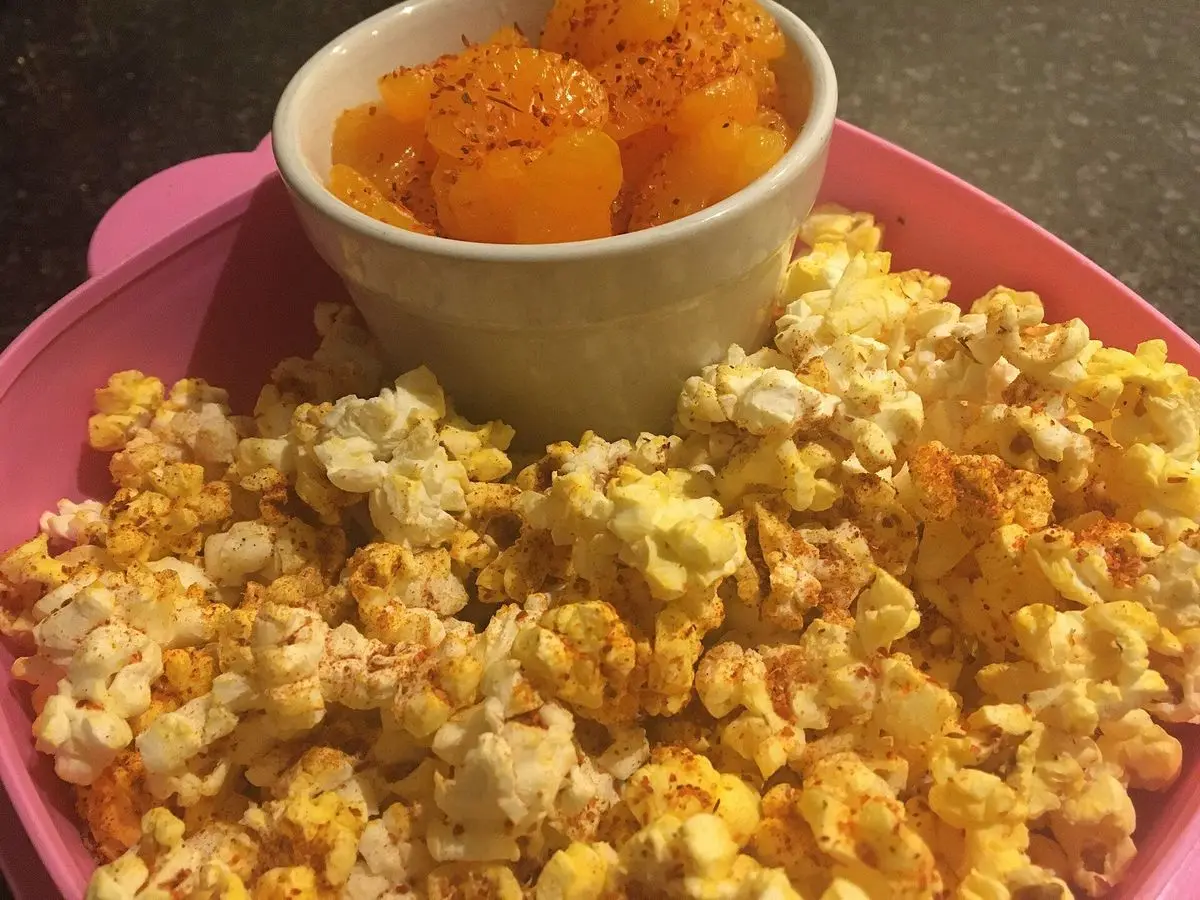 Palomitas de maíz con especias anaranjadas en un cuenco rosa con un pequeño cuenco encima