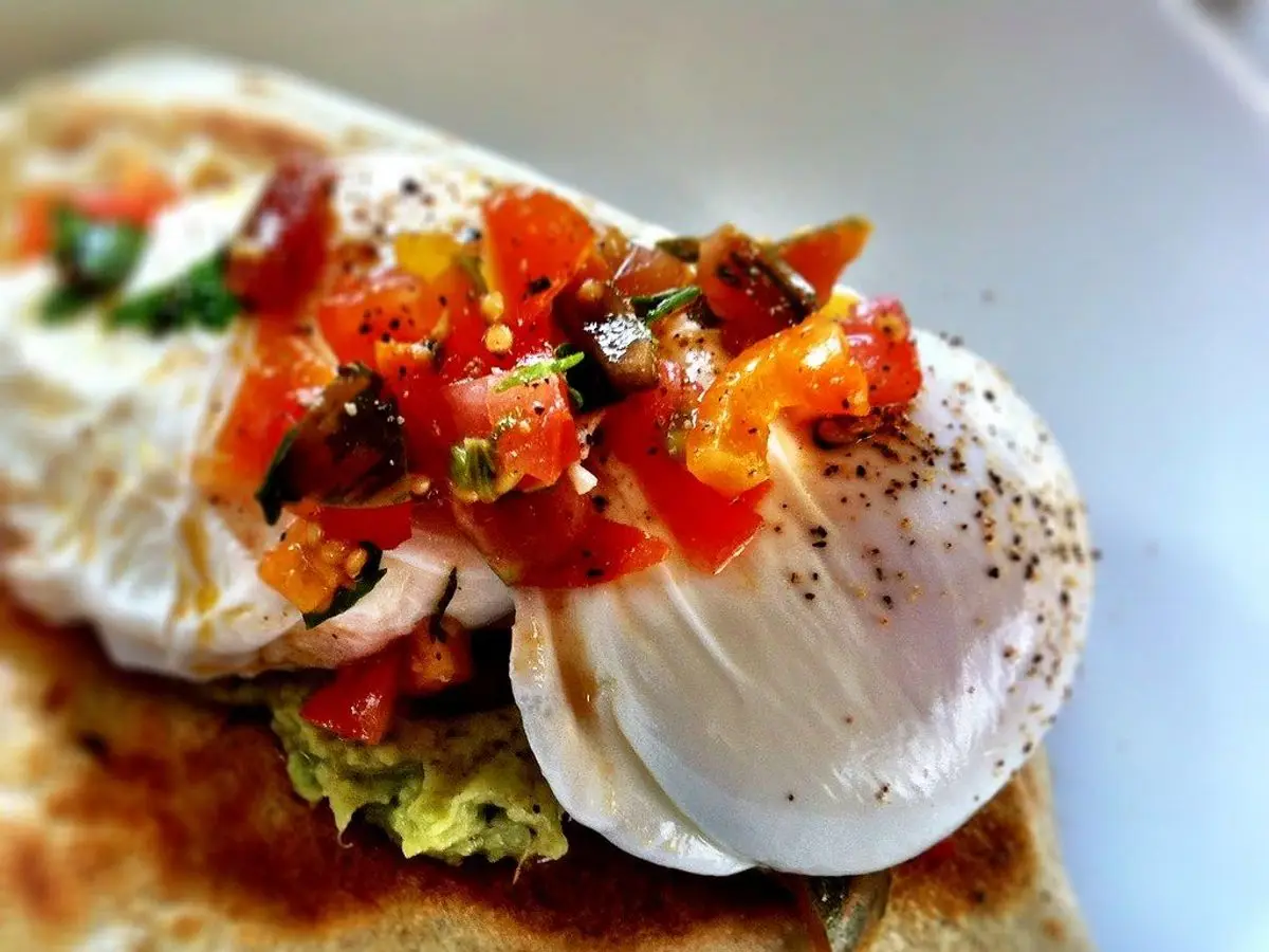 Rebanada de pan tostado con huevos poché, tomate picado y aguacate