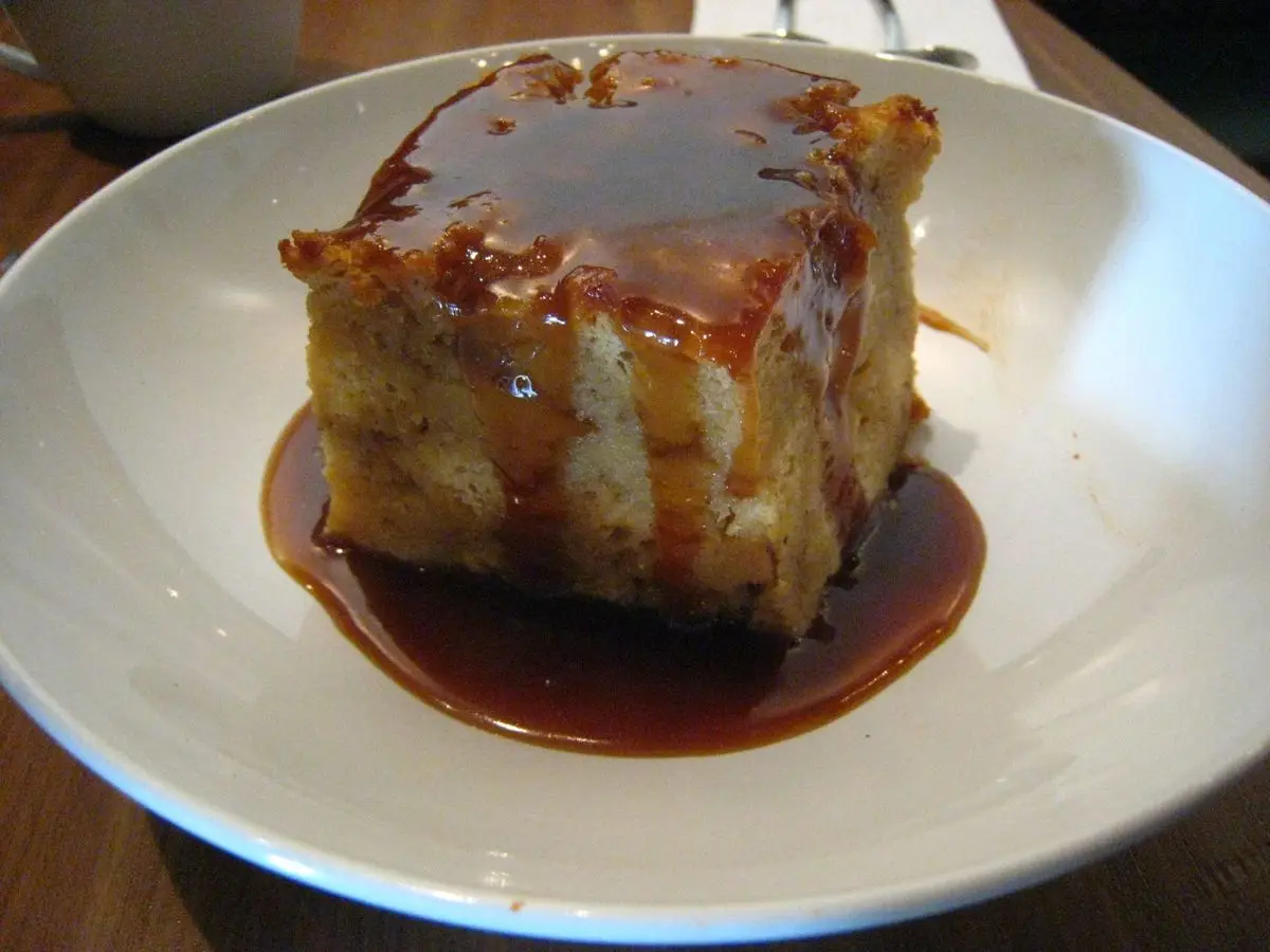 Porción de pudin de pan con salsa de caramelo sobre un plato blanco