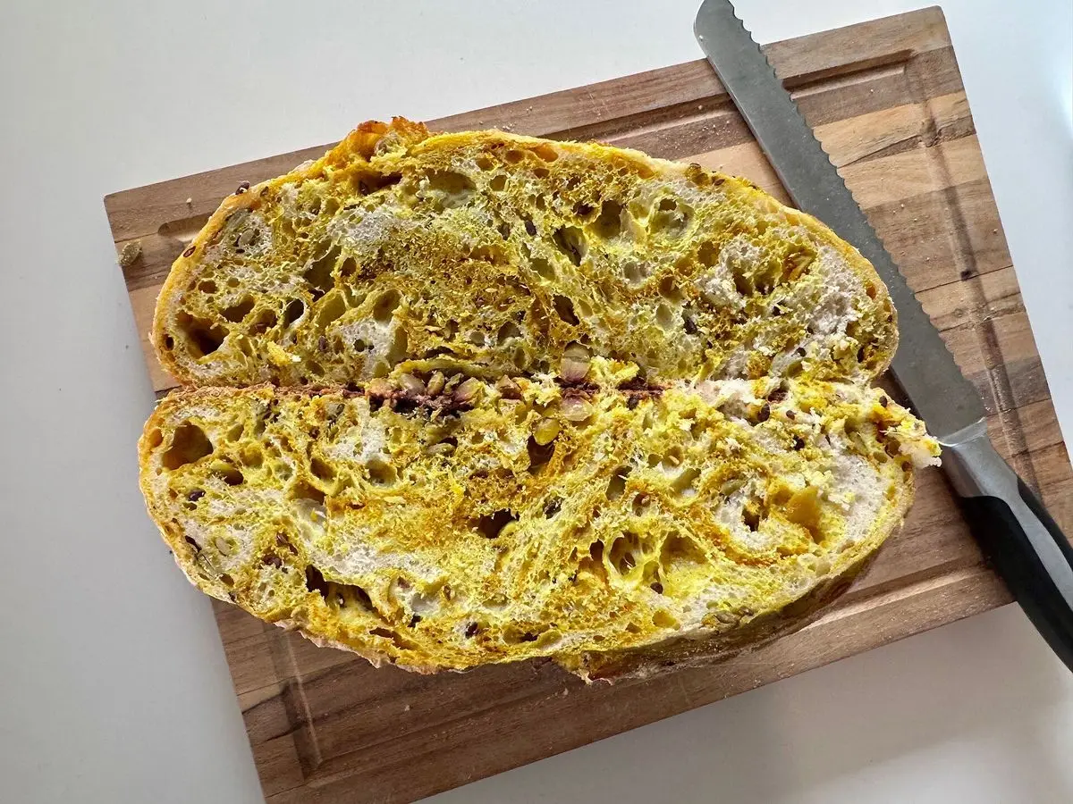 Hogaza de pan de semillas cortada por la mitad sobre una tabla de madera con un cuchillo