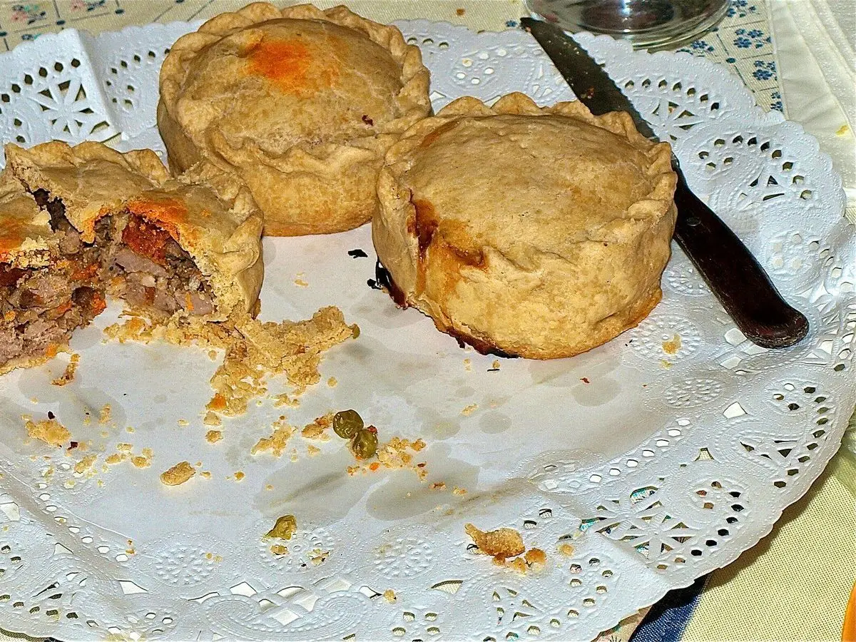 Panades mallorquinas sobre una blonda de papel, una de ellas abierta con relleno de carne