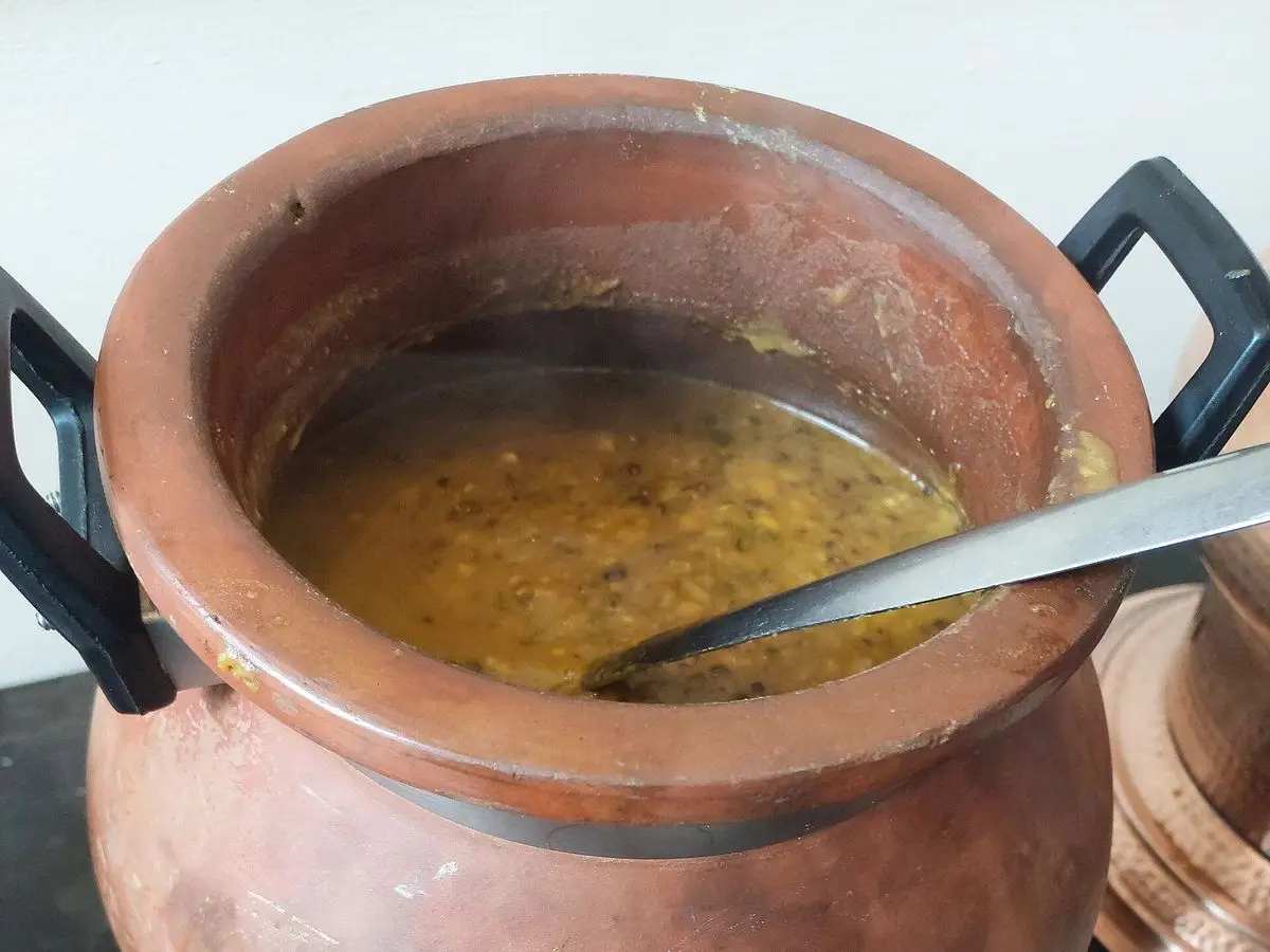 Olla de barro cobriza llena de dal amarillo de legumbres con cucharón