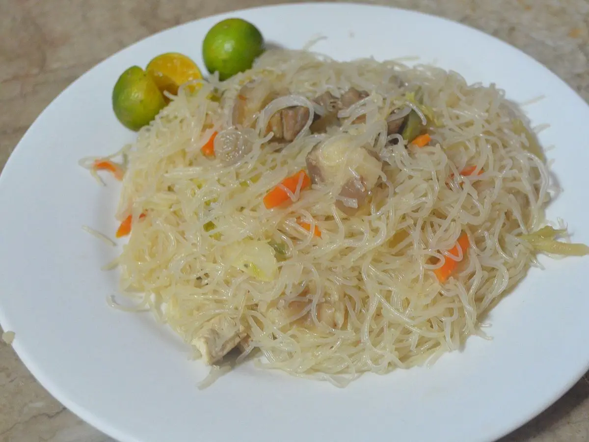 Plato blanco de fideos de arroz finos con zanahoria, carne y verduras y limas pequeñas