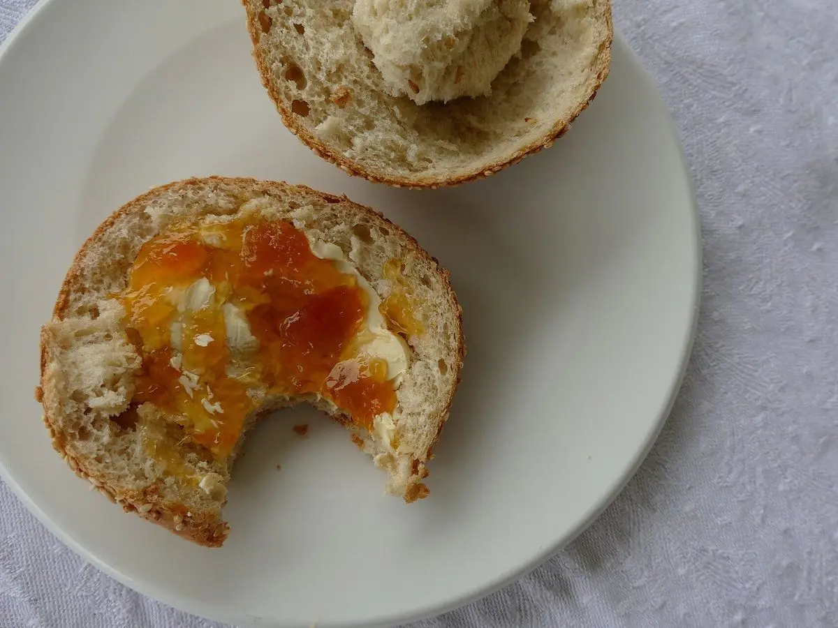 Panecillo cortado por la mitad con mermelada de naranja y queso cremoso sobre un plato blanco