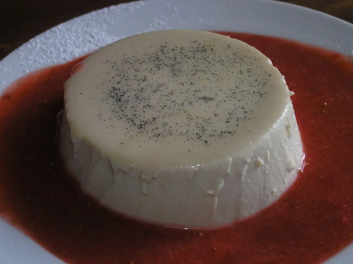Panna cotta blanca con vainilla sobre un coulis rojo de fresa en un plato blanco