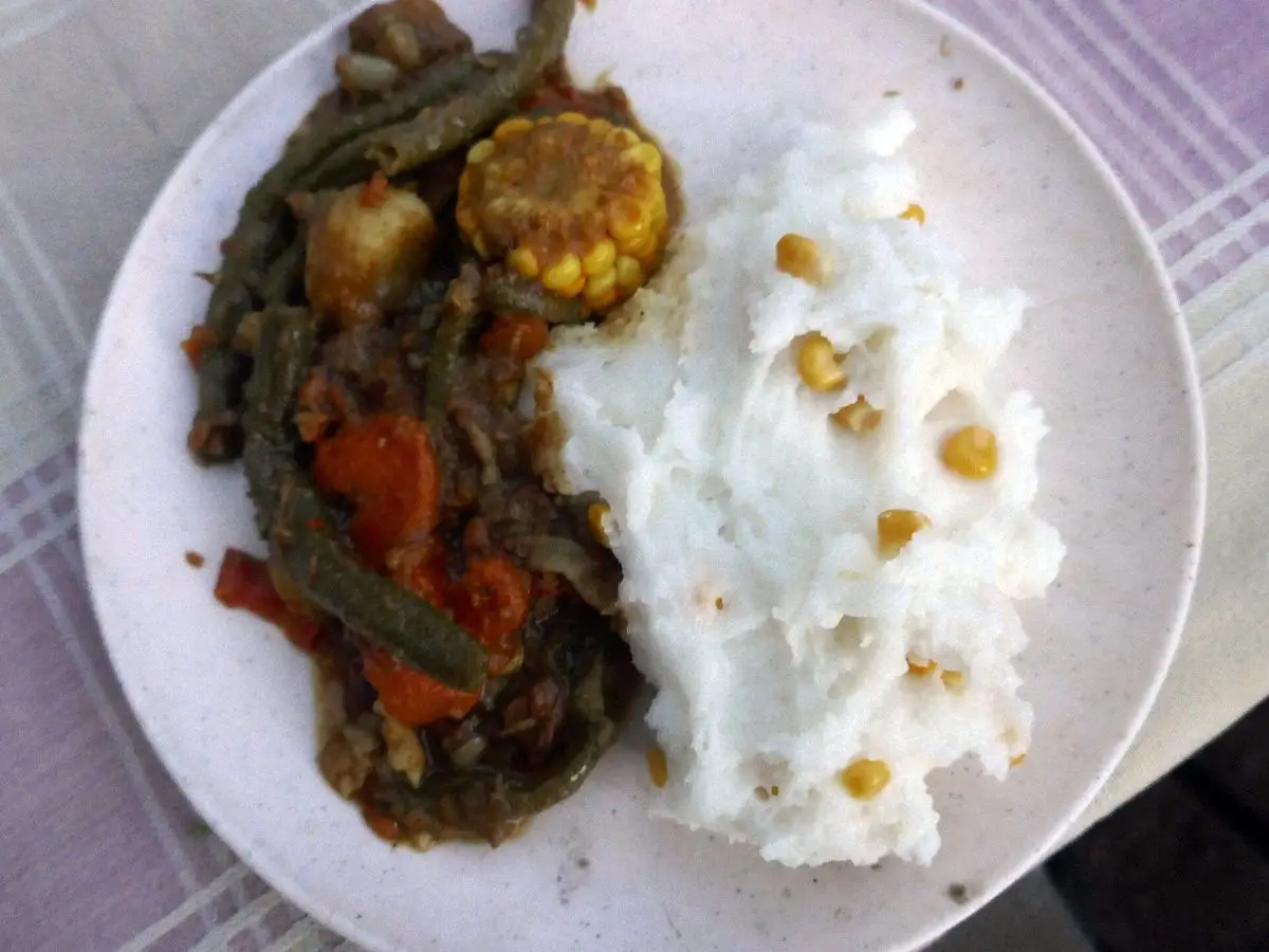 Plato con pap blanco de maíz salpicado de granos y un guiso de judías verdes, zanahoria, patata y mazorca