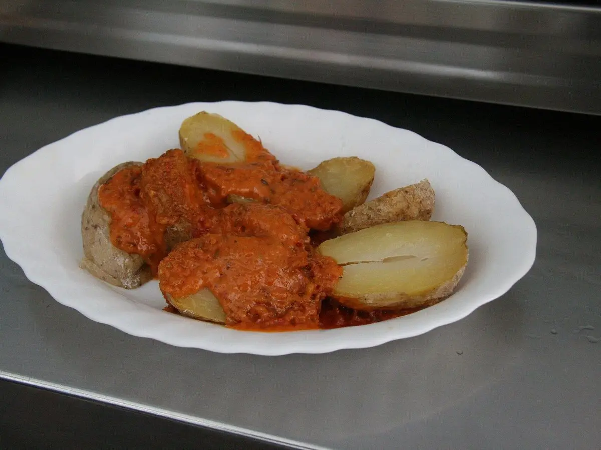Plato de papas cocidas con piel, partidas y cubiertas de una salsa espesa anaranjada