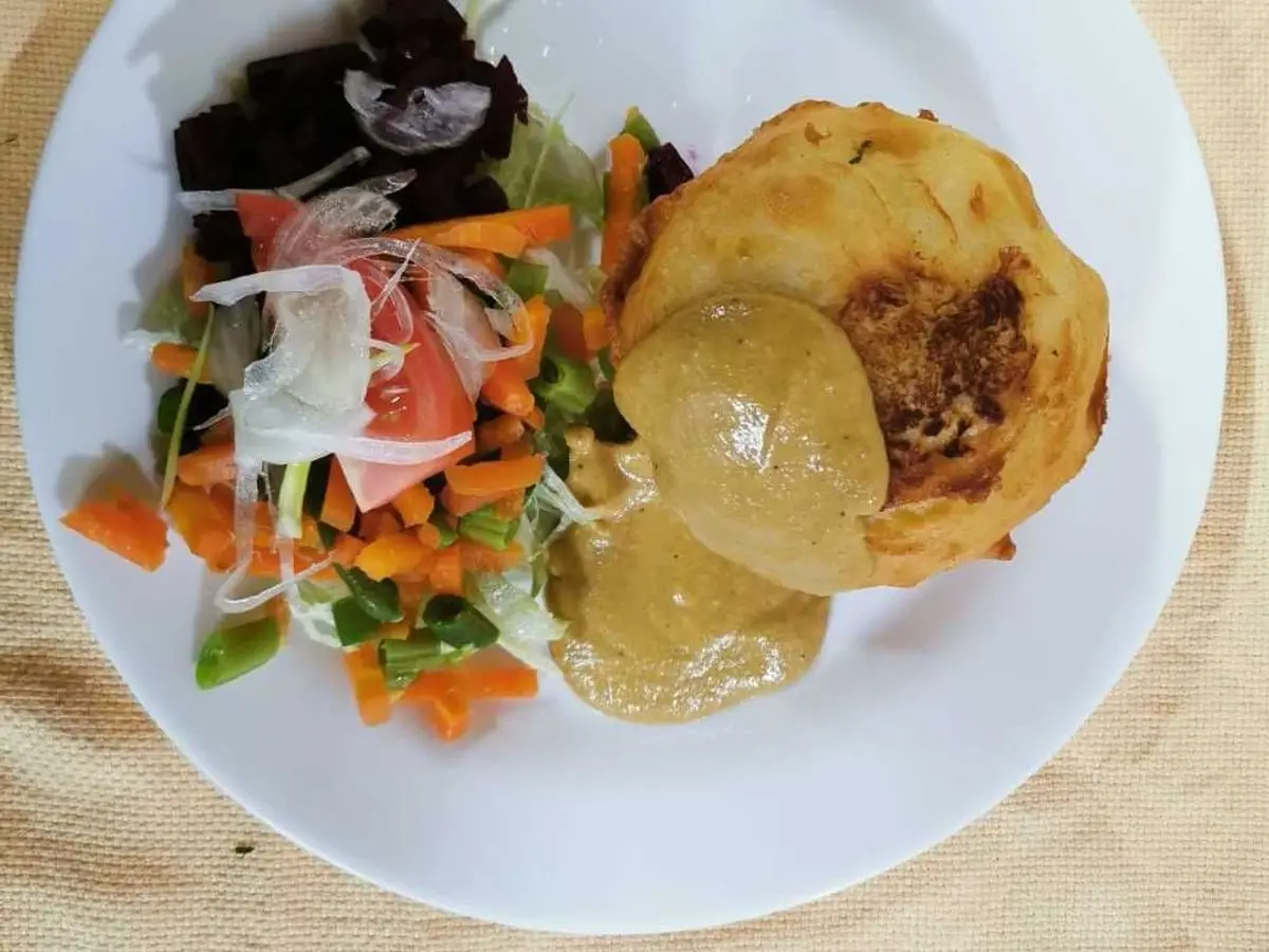 Papa rellena dorada abierta con su relleno, junto a ensalada de cebolla morada y zanahoria en un plato blanco