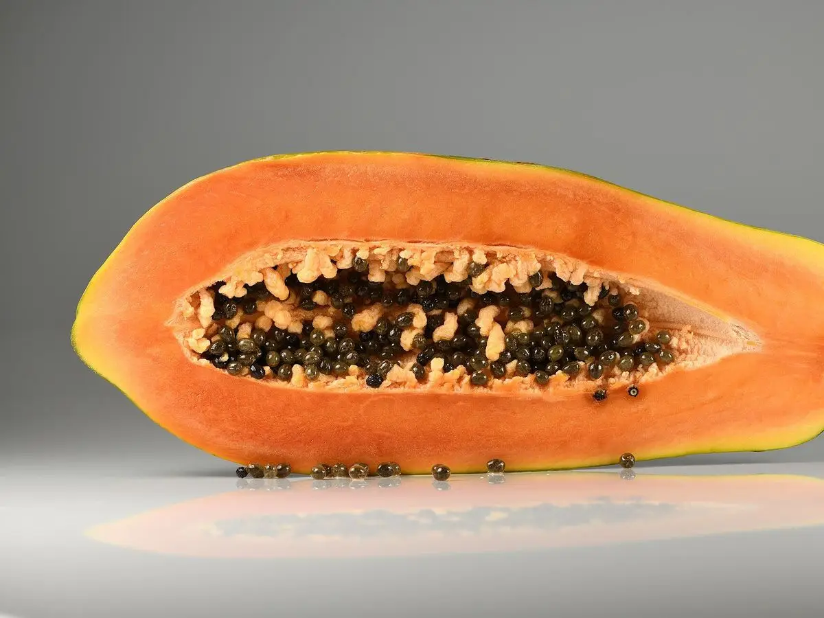 Papaya abierta por la mitad mostrando su pulpa naranja y las semillas negras sobre fondo gris