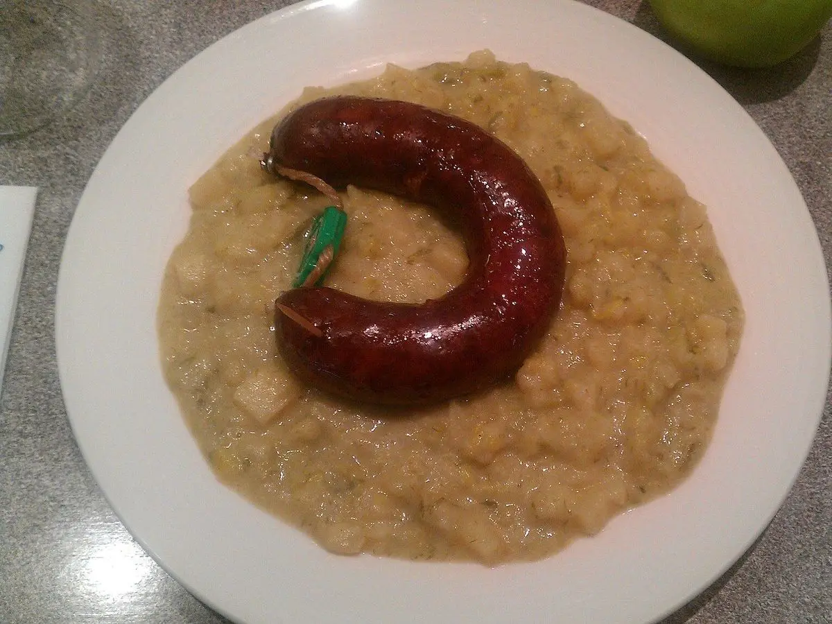 Puré de puerro y patata con una salchicha curvada encima en un plato blanco