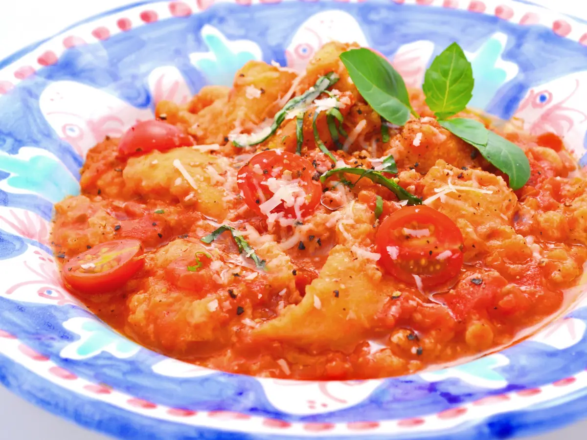 Sopa espesa de tomate y pan con albahaca y queso rallado en un cuenco de cerámica azul