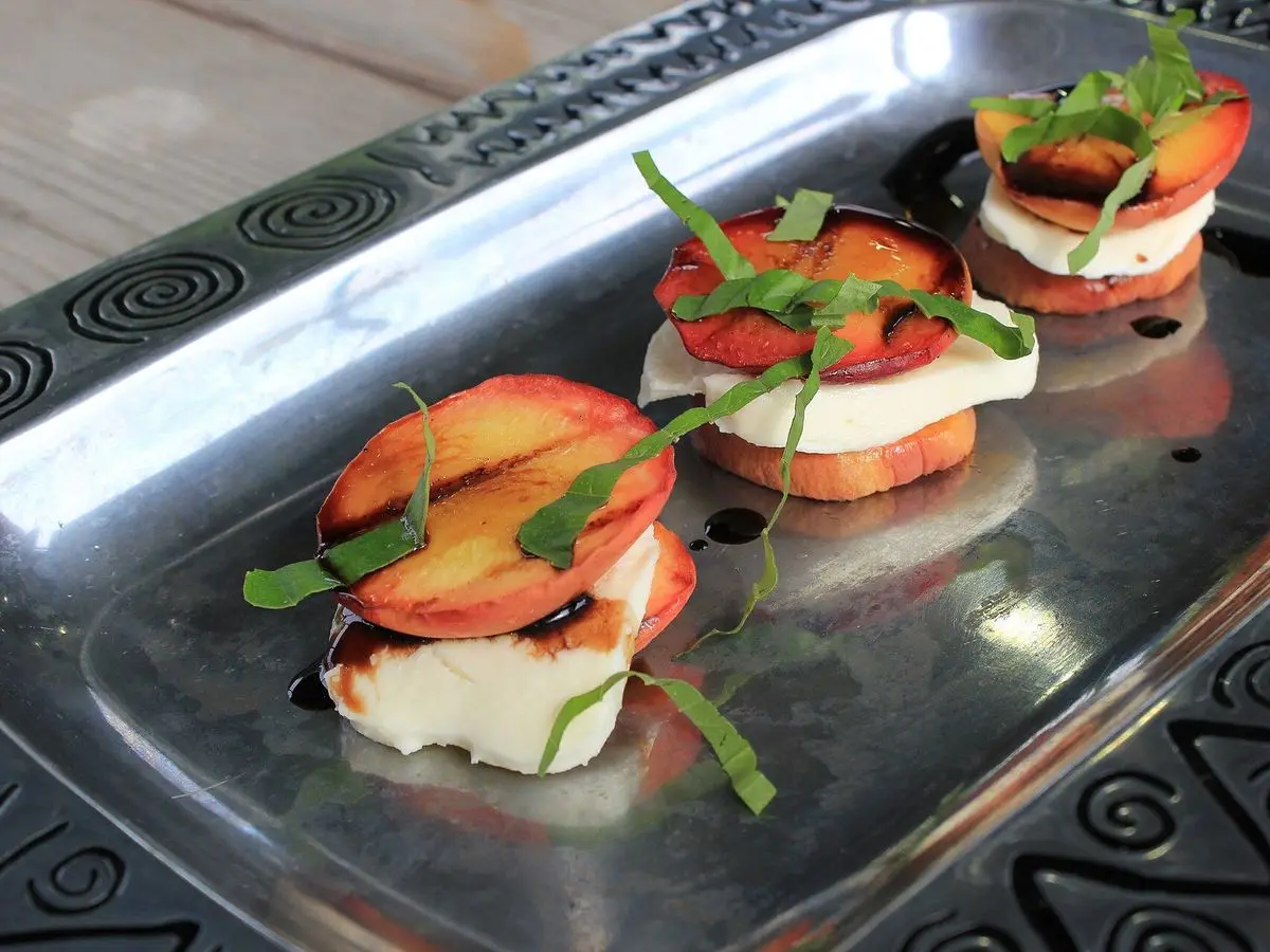Rodajas de melocotón a la plancha con queso fresco, hojas verdes y un hilo de miel
