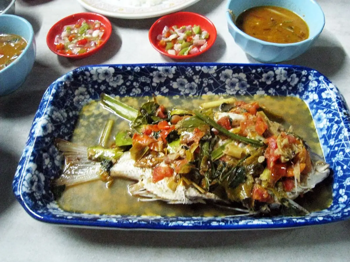 Pargo entero guisado con salsa de tomate, cebolla y hierbas en una fuente azul y blanca