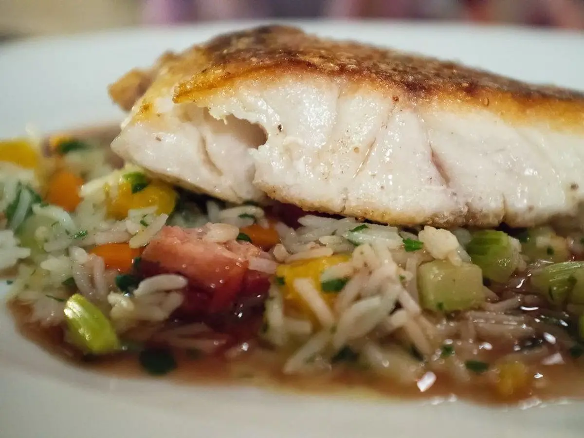 Filete de pargo a la plancha sobre un salteado de verduras en dados y arroz en un plato blanco