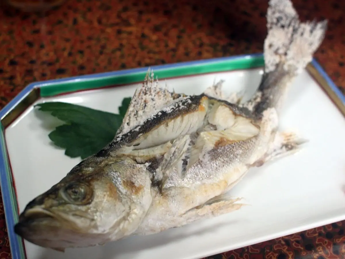 Pargo entero a la parrilla servido sobre una bandeja blanca con hojas verdes