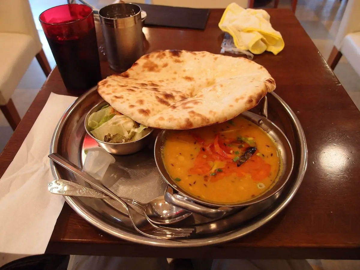 Bandeja metálica con cuenco de dal anaranjado, pan naan y pequeños platos de acompañamiento