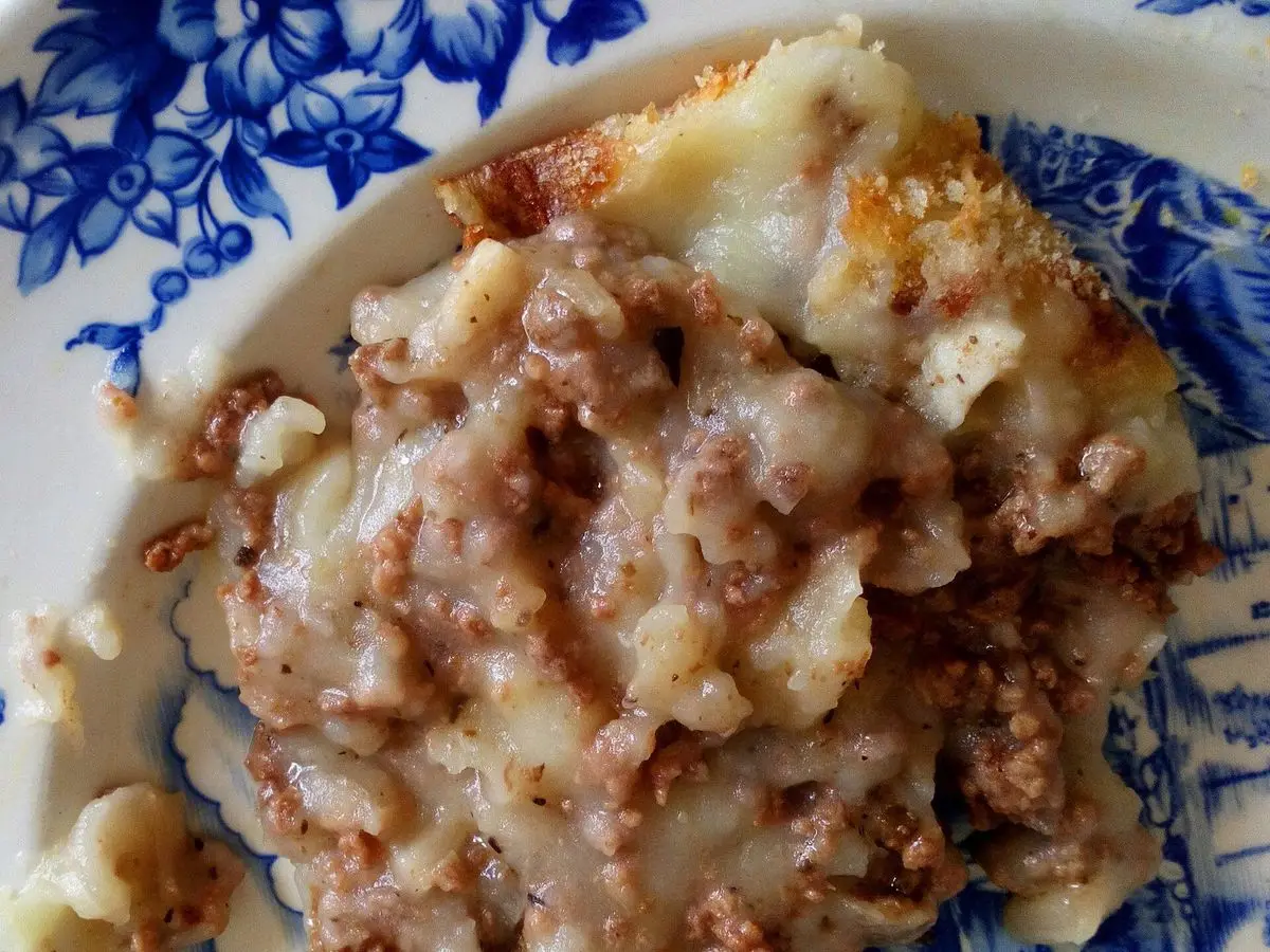 Ración de parmentier de carne picada con puré de patata gratinado en un plato de motivos azules