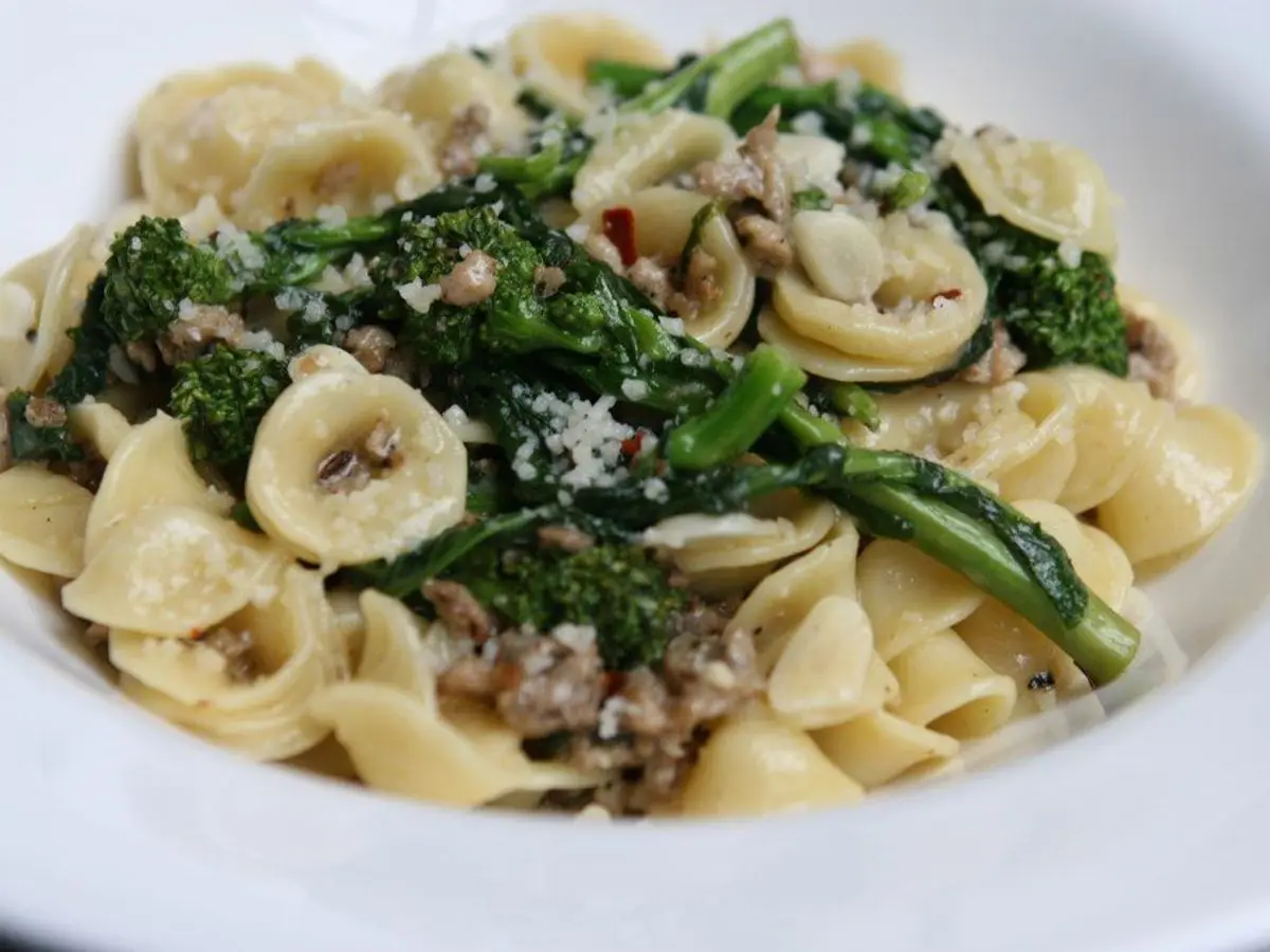 Orecchiette con brócoli rabe y salchicha desmenuzada, espolvoreadas con queso en un plato blanco