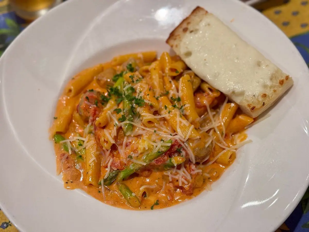 Pasta corta con salchicha y salsa de tomate anaranjada con hierbas en un plato blanco