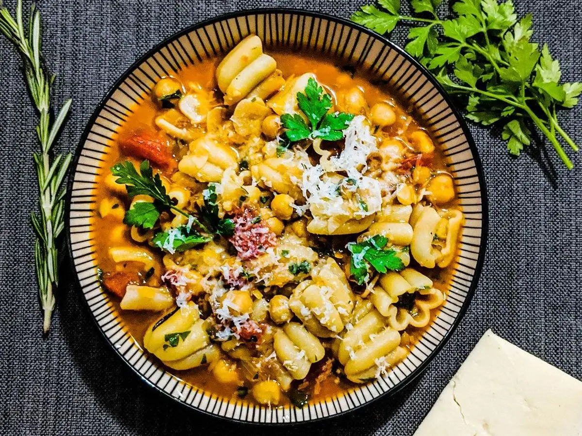 Cuenco de pasta con garbanzos y perejil en salsa de tomate sobre un mantel oscuro