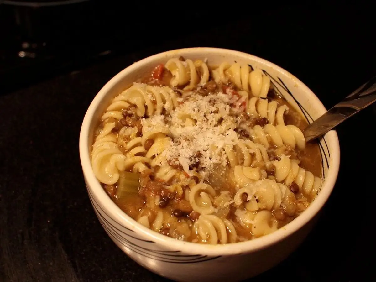 Cuenco de pasta en espiral con sopa de lentejas y verduras con queso rallado