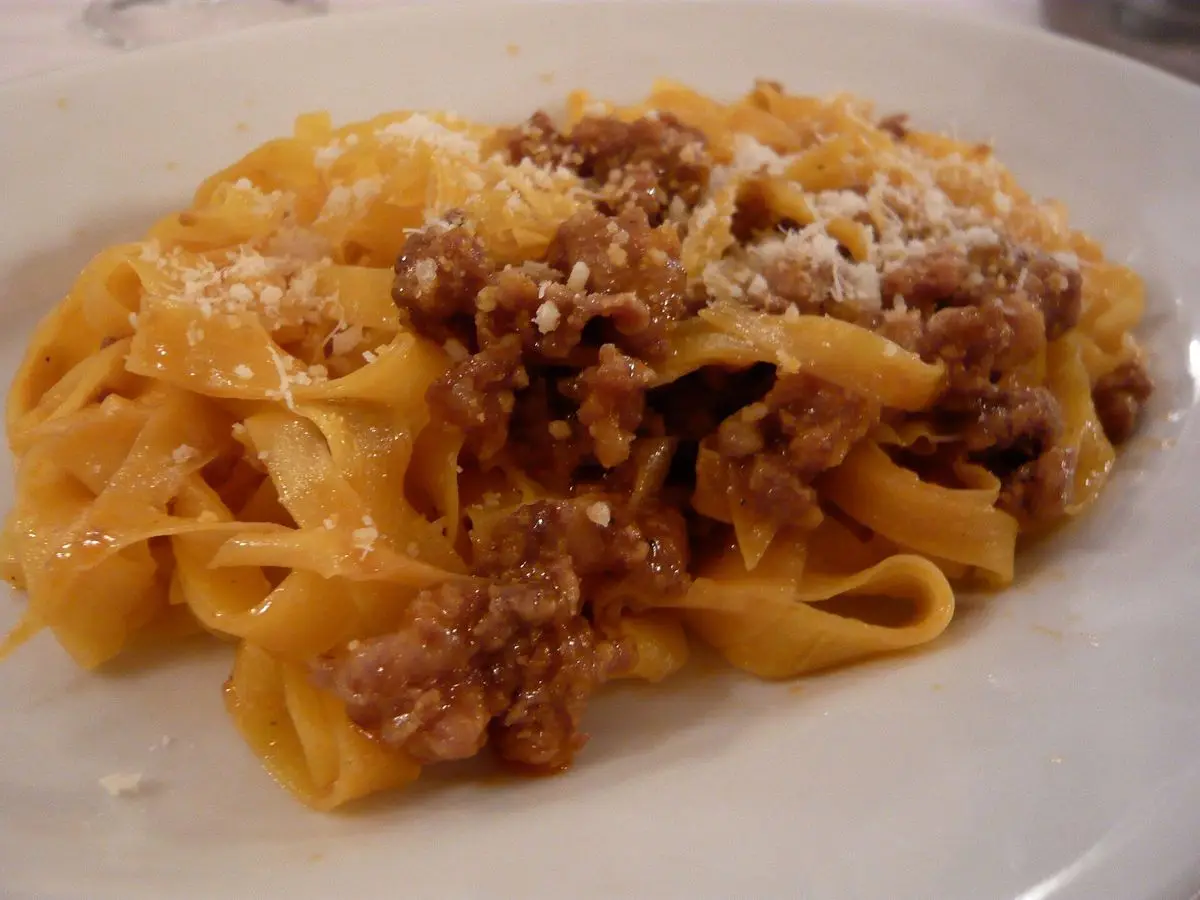 Tagliatelle frescas al huevo con ragú de carne y queso rallado en un plato blanco