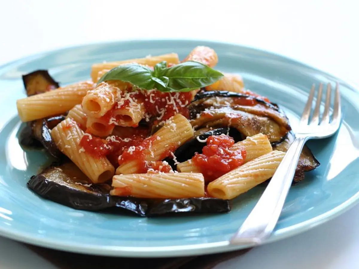 Plato azul de pasta penne con berenjena frita, tomate y albahaca