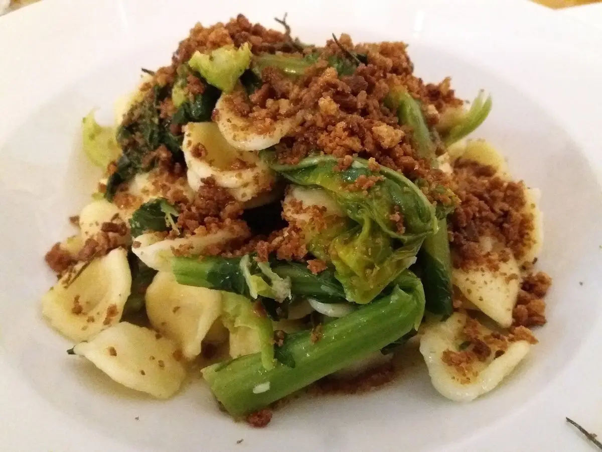 Orecchiette con verduras verdes y migas de pan tostado en un plato blanco