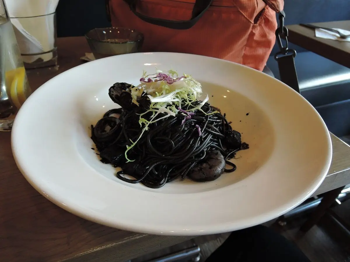Plato blanco de pasta negra con tinta de calamar y marisco, con un toque verde por encima