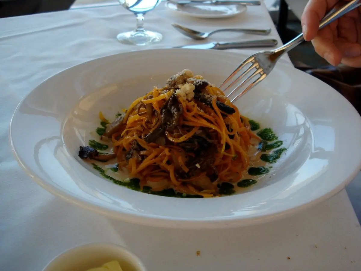 Plato hondo de espaguetis con salsa anaranjada y hojas verdes