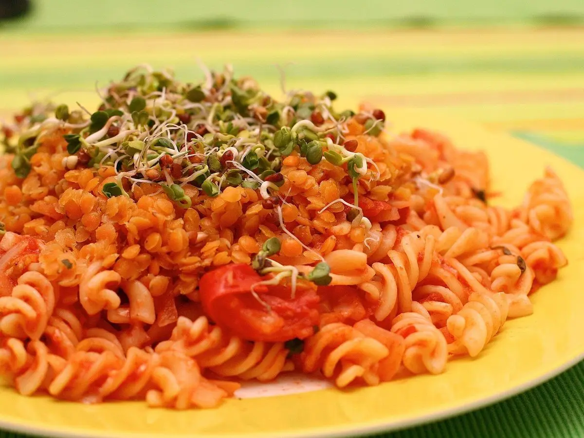 Plato amarillo de pasta de lentejas en espiral con salsa de tomate y brotes