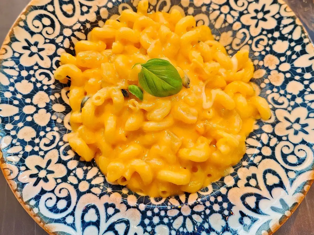 Pasta con patatas y queso fundido cremosa con una hoja de albahaca en un plato de cerámica azul