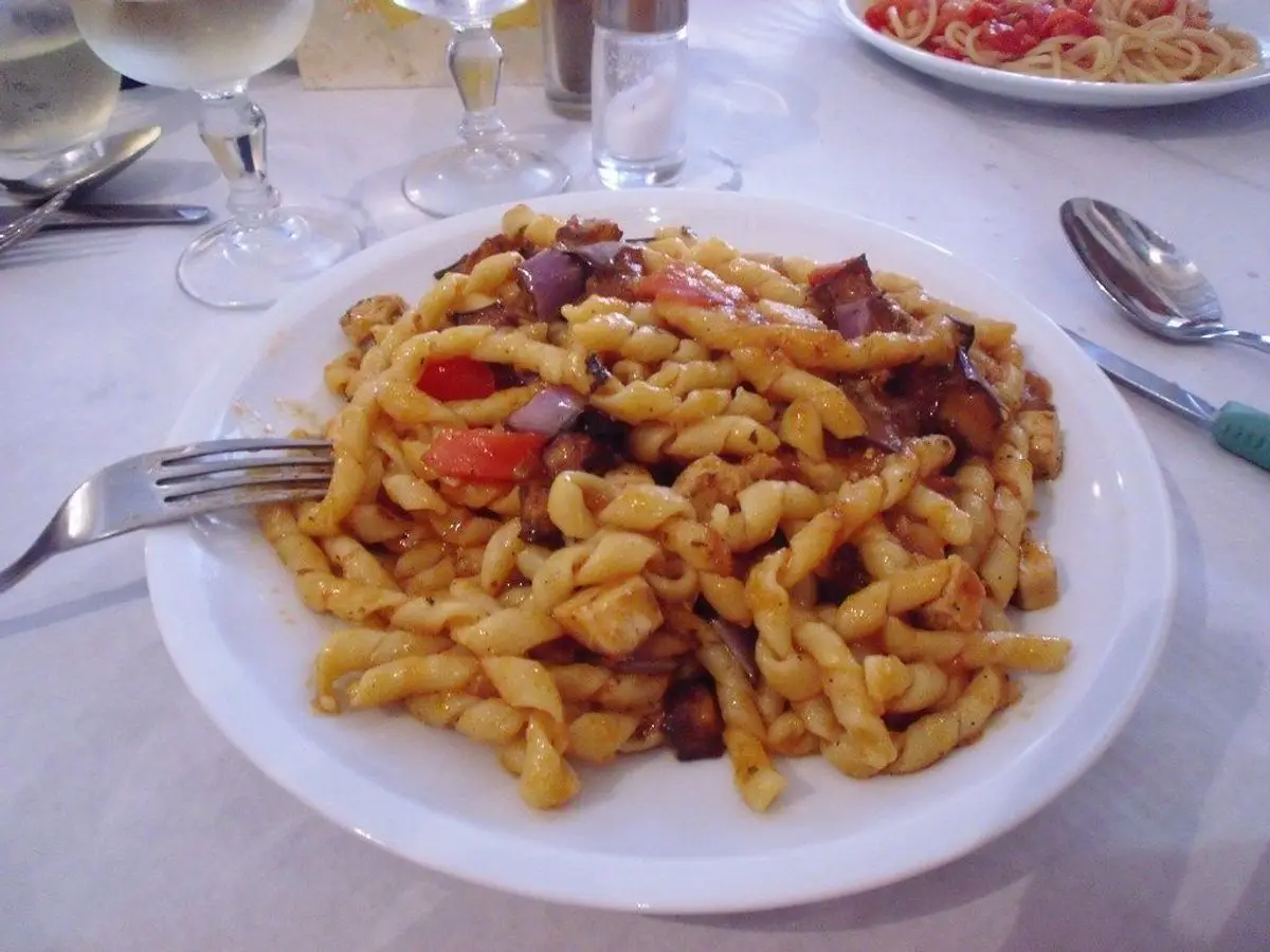 Plato de pasta corta con salsa de tomate y trozos oscuros de verdura