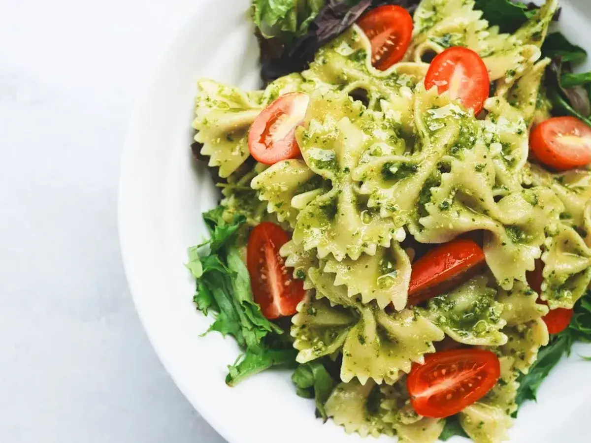 Pasta lazo con pesto, tomates cherry partidos por la mitad y hojas verdes en un plato blanco