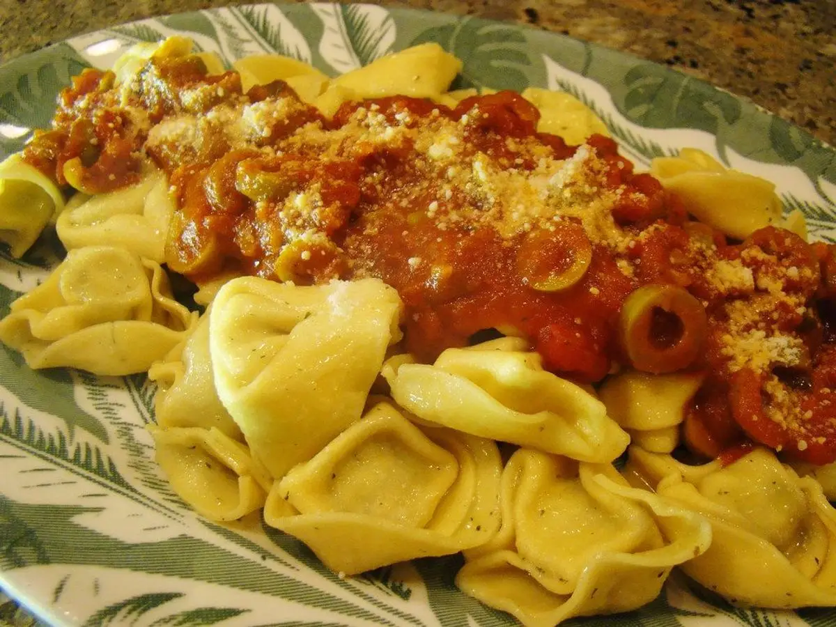 Tortellini rellenos con salsa de tomate y aceitunas en un plato con borde verde