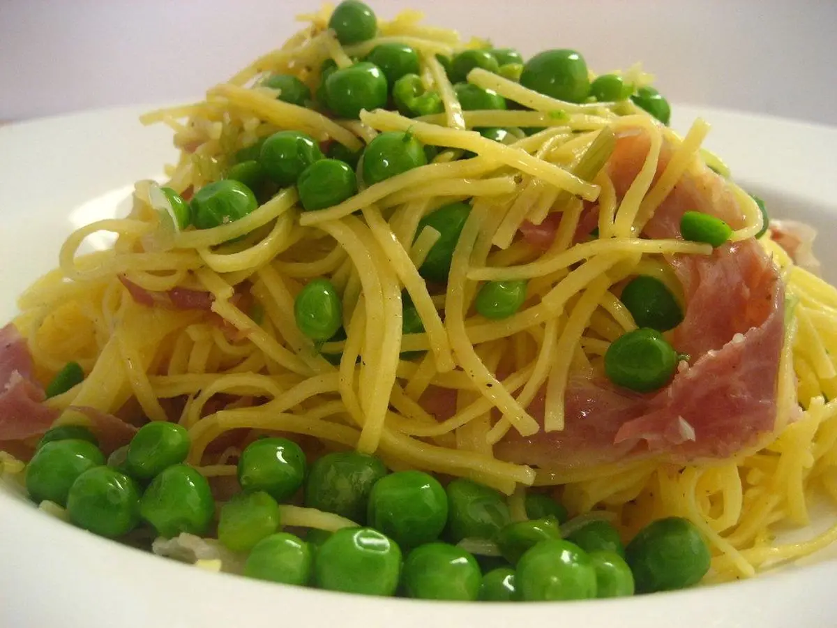 Espaguetis con guisantes verdes y lonchas de jamón en un plato blanco