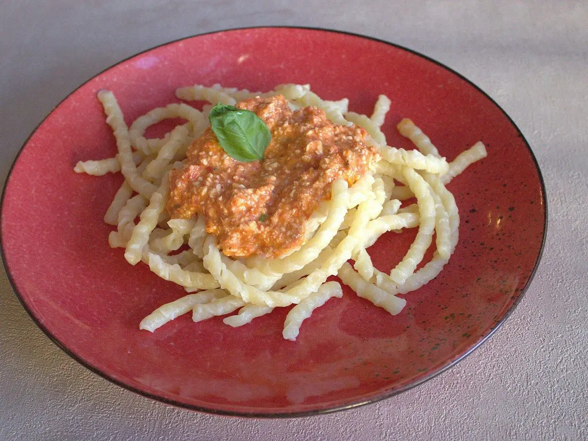 Plato rojo de pasta con salsa de tomate y almendra anaranjada y una hoja de albahaca